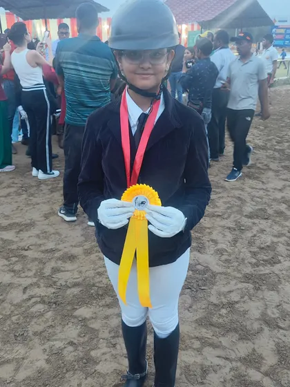 The smile of a champion. This young rider proudly displays her ribbon after a great performance, showing the joy that comes with equestrian sports.