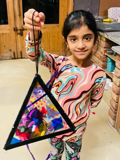 A student proudly holds up the triangular lantern she made in our Diwali art workshop. The piece is a beautiful collage of colors and textures.