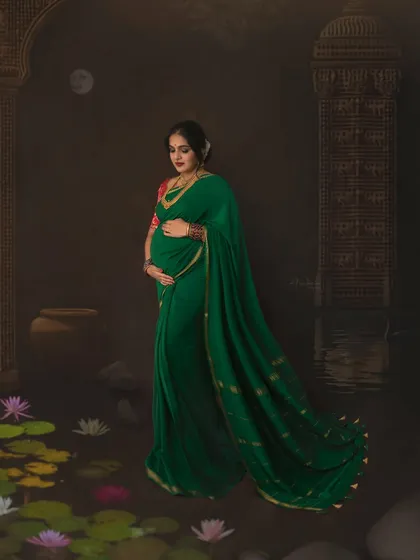 This full-length portrait captures the graceful flow of the green saree, adding a sense of movement and elegance. The artistic backdrop with the moon and temple pillars enhances the storytelling element of this conceptual maternity shoot.