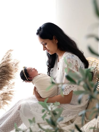 A serene moment with mom holding her newborn baby girl in our boho studio setup. The natural light and textures create a peaceful and beautiful portrait.