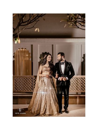 A classic, full-length shot of the couple, her in a sparkling lehenga and him in a sharp tuxedo, the epitome of reception glamour.