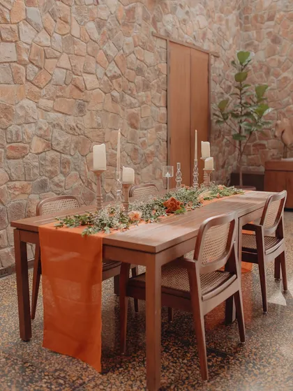 An indoor dining table is set with a vibrant orange runner and a simple green centerpiece. This shows how we can bring color and life to our indoor spaces as well.