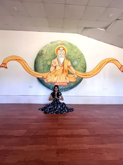 A wider view of my meditative pose in Mysore, showing the beautiful mural and the spacious, calming environment that inspires me.