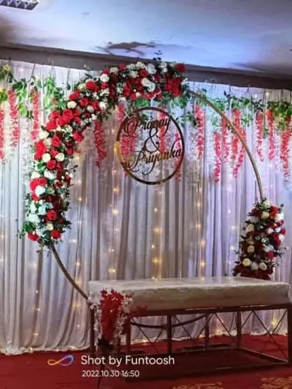 A full view of the red and white themed engagement stage. The setup includes a metal arch, white drapes with fairy lights, and hanging wisteria flowers.