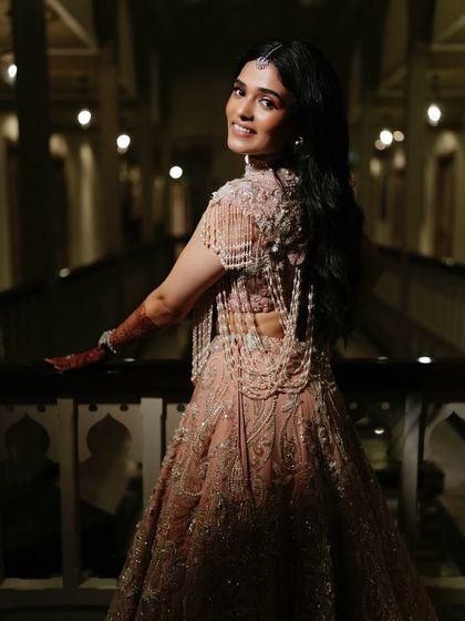A view from the back, showing the stunning pearl-draped blouse and the bride's radiant smile. The makeup is flawless from every angle.