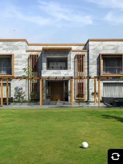 A full view of the renovated farmhouse facade, featuring natural stone cladding and wooden louvers for privacy. The design integrates the home with its natural surroundings while maintaining a modern aesthetic.