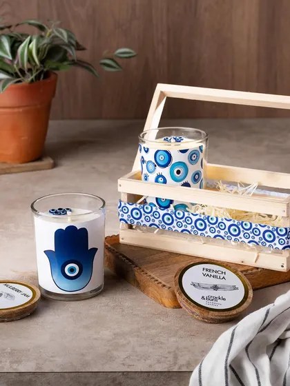 The complete evil eye gift set, featuring a Hamsa Hand candle, a patterned glass jar candle, and a decorative wooden crate.
