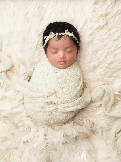 A beautifully simple portrait of a newborn swaddled in a cream-colored wrap on a soft, fluffy surface. Sometimes, simplicity is the most elegant way to capture a baby's beauty.