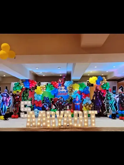 An epic superhero stage setup for a birthday celebration. This wide shot shows a full stage decorated with multiple life-size superhero cutouts and marquee letters spelling out the birthday boy's name.