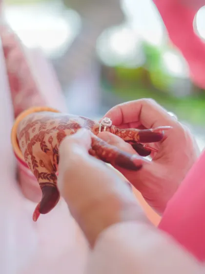A close-up of the ring exchange ceremony. This shot focuses on the hands, the intricate mehendi, and the wedding ring, symbolizing the official union of the couple.
