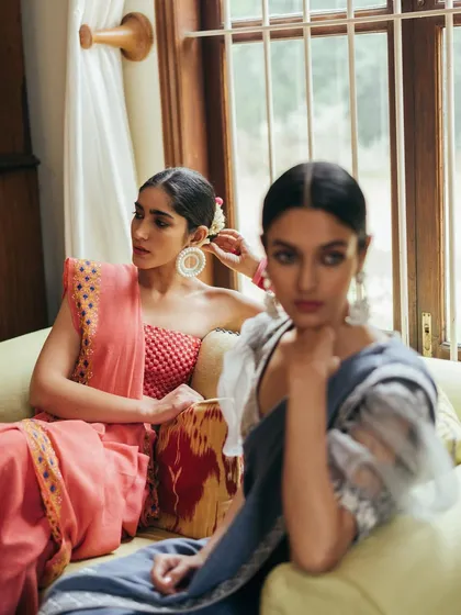 A dual-model shot from an indoor lookbook. The focus is on the model in the background, while the foreground model is softly blurred, creating depth and a candid feel.