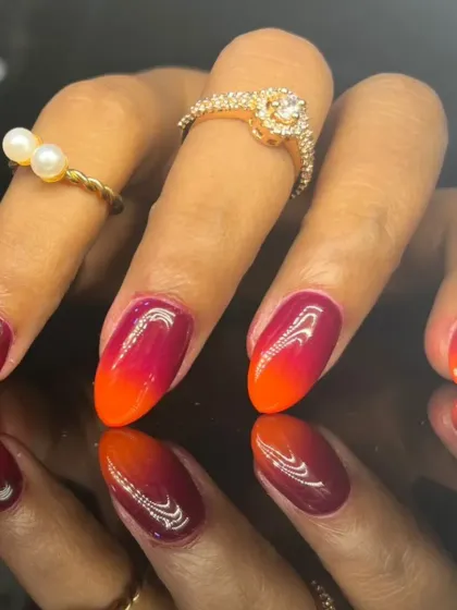 A fiery ombre design blending deep burgundy into a vibrant orange-red on almond-shaped nails.