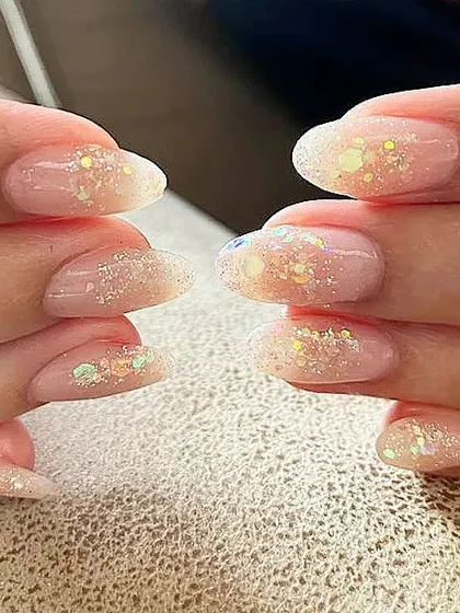 A close-up of sheer nails with embedded iridescent glitter, showing how they catch the light.