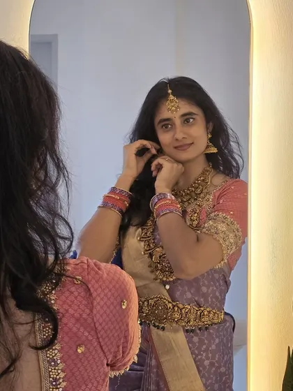 Adjusting her earring, Laasya's reflection captures the quiet moments of preparation for a special occasion.