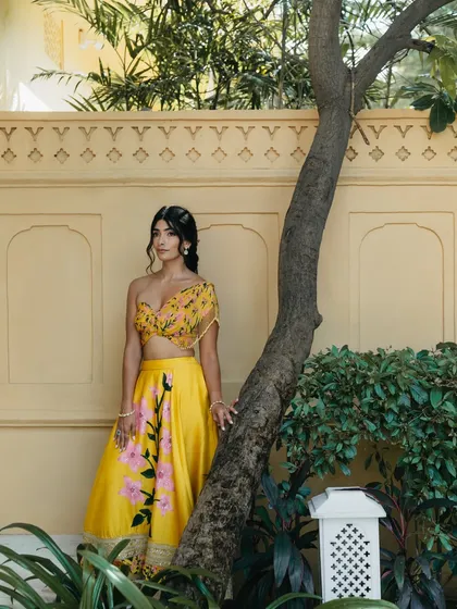 A serene bridal portrait against a yellow wall in Rajasthan. The bride's pose is relaxed and natural, capturing a moment of calm during the Mehendi celebrations.