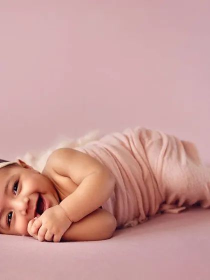 A happy baby girl lying on her side during her 4-month milestone session. Her bright smile and cheerful expression are simply infectious.