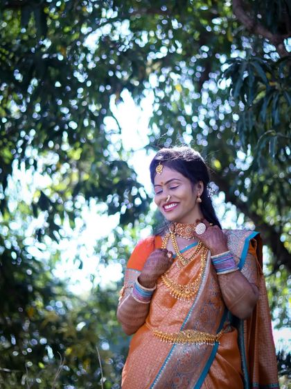 An outdoor portrait capturing a happy moment. The model is dressed in a beautiful orange saree, with the natural green background making the colors stand out.