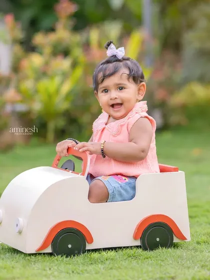 A happy toddler enjoying a ride in a miniature car on a lush green lawn. Outdoor sessions like this are great for capturing energetic and natural moments.