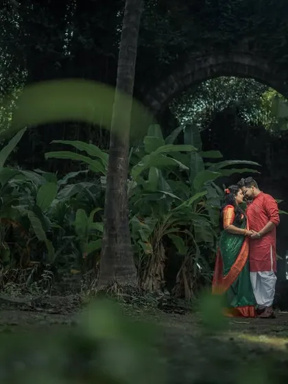 A romantic pre-wedding portrait of a couple framed by lush greenery in a historic fort setting.