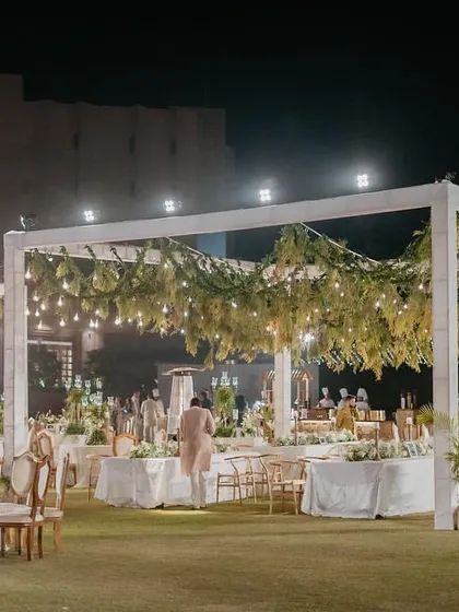 An elegant dinner setup under a canopy of greenery and lights for the 'Luxe Garden' wedding.