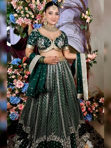 A model posing in a deep green lehenga with silver embroidery. This is a rich and elegant color choice for a winter wedding.