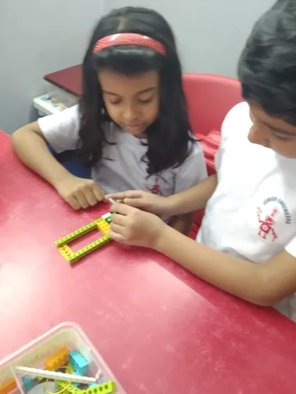 Two children work together, with one guiding the other on how to connect a piece for their LEGO model.