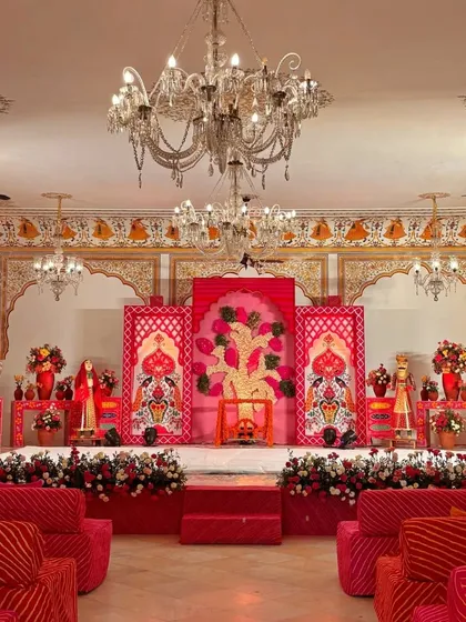 A grand indoor setup with a red and pink color scheme. The stage features a 'Tree of Life' backdrop, and the room is filled with royal seating and elegant chandeliers.
