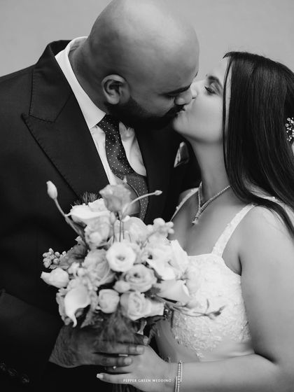 A classic black and white portrait of the couple sharing a kiss, the bouquet adding a beautiful textural element. A timeless and romantic shot.