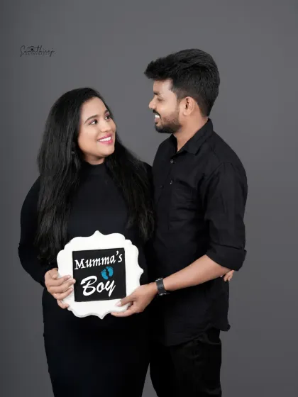 A happy couple portrait announcing "Mumma's Boy." Their matching black outfits and the cute sign create a sweet and personal gender reveal photo.