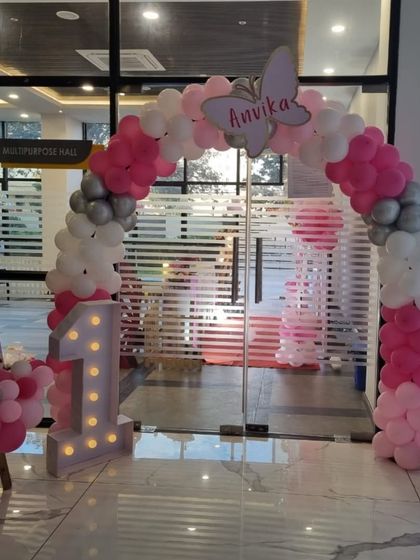 A beautiful entrance for a butterfly-themed first birthday, featuring a pink, white, and silver balloon arch and a large light-up number '1'.