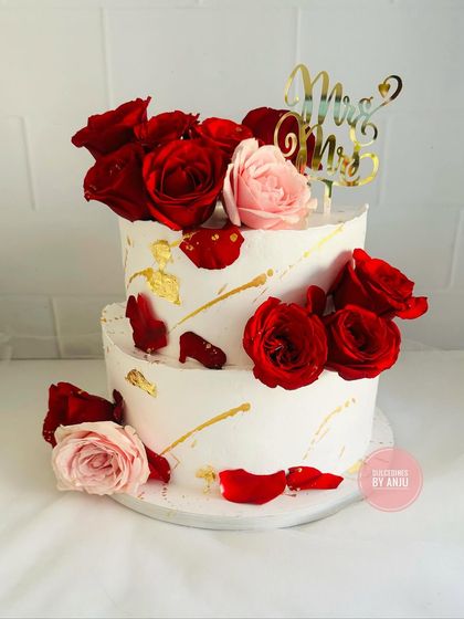 A passionate and romantic two-tier wedding cake. The abstract gold leaf strokes and scattered fresh red roses give this design a modern, artistic feel.