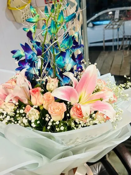 A premium hand-tied bouquet featuring vibrant blue orchids, soft pink lilies, and delicate peach roses. This is a great choice if you want a modern and elegant flower arrangement.