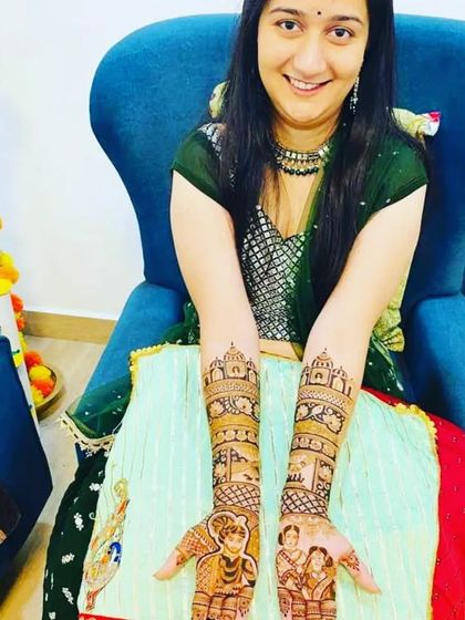 A smiling bride displays her beautiful portrait mehendi, featuring a groom on a horse and a bride in a doli, capturing the classic baraat theme.