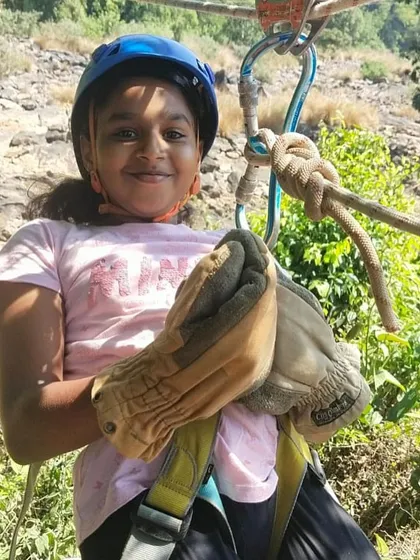 A close-up of a young girl, fully harnessed and gloved, ready for her turn on the rope course.