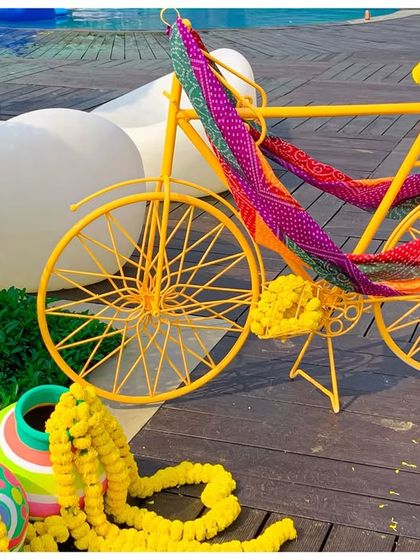 A quirky decor element for the Holi party: a bright yellow bicycle decorated with colorful bandhani fabric and marigold garlands.