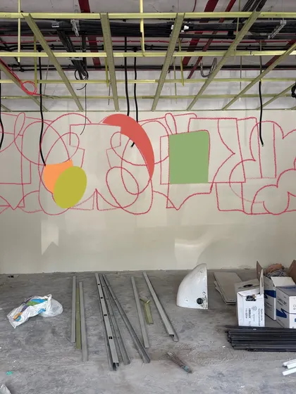 The very beginning of the 42-foot mural, with initial sketches and color blocks on the wall of a raw construction site. This illustrates the transformation from a blank space to a vibrant work of art.