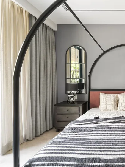 The centerpiece of this master bedroom is the majestic bed with its grand, curved metal frame. Paired with a muted grey wall color and warm pink upholstery, it creates a look that is both regal and contemporary.