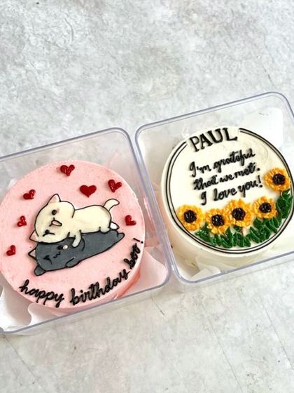 Two adorable mini bento cakes, one with a sweet message and sunflowers, and another with two cats cuddling.