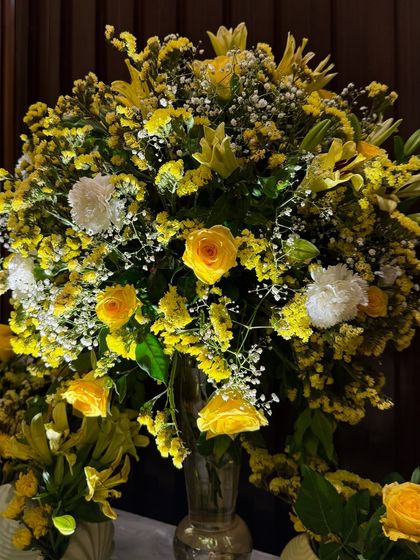 A close up of a lush floral arrangement from the wedding. This bouquet is filled with vibrant yellow roses, lilies, and white carnations, adding brightness and joy to the decor.