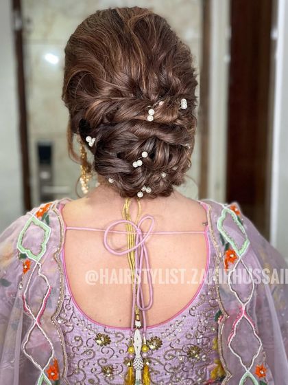 A voluminous updo with interwoven sections, decorated with scattered pearls. This hairstyle adds height and texture, making it a glamorous choice for an evening reception.