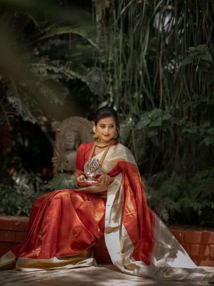 The full drape of the red and off-white Kanchipuram silk saree is displayed here, showing its luxurious fall and the richness of the handwoven fabric.
