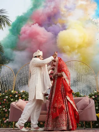 A truly explosive moment of celebration. This Varmala ceremony is punctuated by a vibrant burst of colored smoke, creating a dramatic and unforgettable photo opportunity for the couple.
