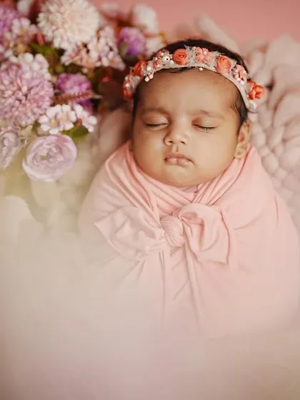 An artistic close-up of a newborn, with a soft, hazy foreground that draws all the attention to her peaceful face and delicate floral headband.