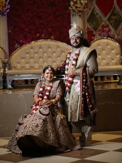 This couple looks regal and perfectly coordinated for their wedding day. The groom is wearing a beige sherwani with a contrasting maroon velvet dupatta.