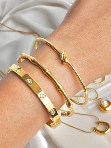 Showcasing a stack of gold-toned bangles on a model's wrist. The soft, silky background adds a touch of luxury, while the focus remains on the texture and shine of the jewellery.