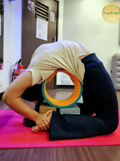The yoga wheel can be a transformative tool for backbends. Here, a student uses the wheel and blocks to support a deep Kapotasana, or Pigeon Pose, opening her heart and spine with control.
