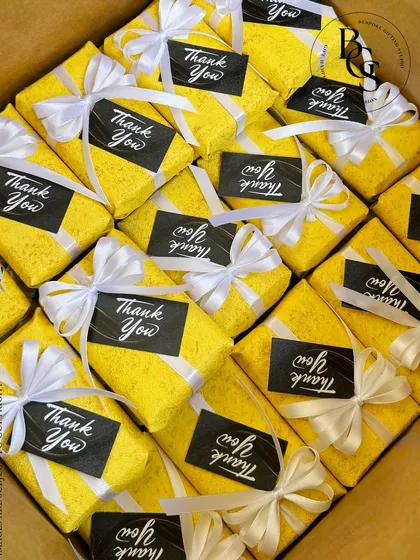A box full of cheerful "Thank You" gifts. Each one is wrapped in bright yellow textured paper, tied with a crisp white ribbon, and finished with a bold black and white thank you tag.