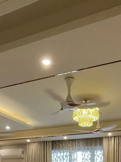 The false ceiling design incorporates both recessed lighting and a statement chandelier, allowing for different lighting moods. The metal cladding adds a sleek, modern edge.