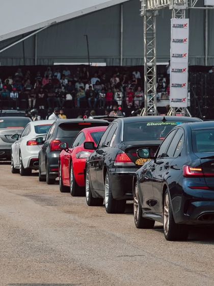 A long line of performance sedans, including BMWs and Audis, queuing up for the race. The paddock area is always buzzing with anticipation and the sight of incredible machinery.
