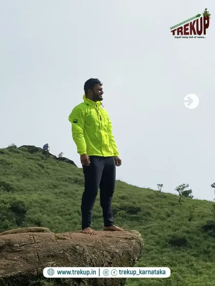 A trek leader standing proudly on a rock outcropping on the Bandaje trail, overlooking the green landscape.